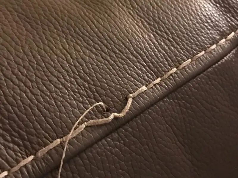 An artisan's hand stitching a leather label onto a carpet